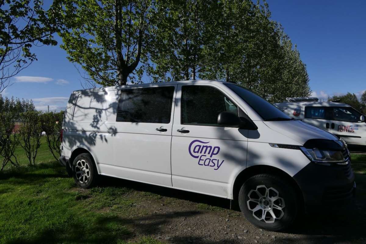 White CampEasy campervan parked under the shade of trees in a lush green park, ideal for a relaxing outdoor getaway in Iceland.
