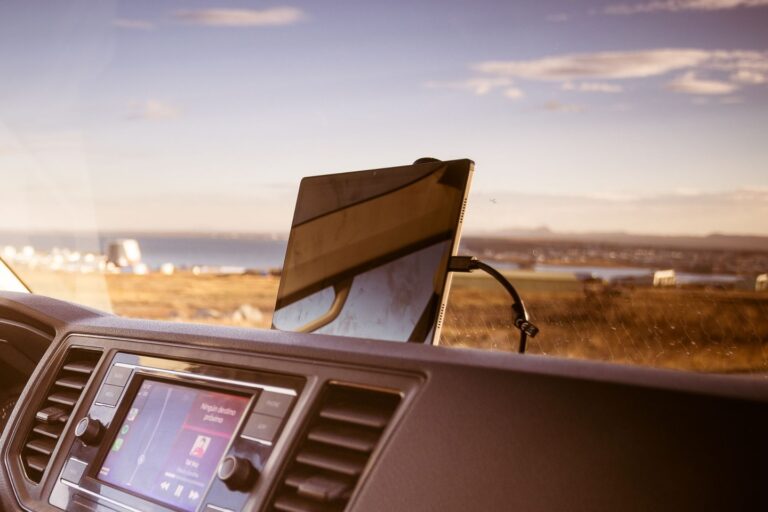A tablet mounted inside a campervan in Iceland, displaying navigation, with a scenic coastal view in the background.