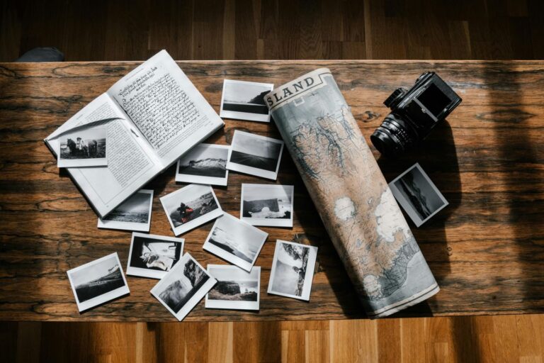A wooden table with an open book, vintage camera, Iceland map, and scattered black-and-white travel photos.