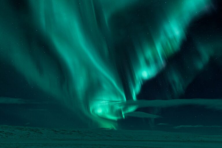 Northern lights glowing in the Icelandic night sky, creating a magical green aurora over a snowy landscape.