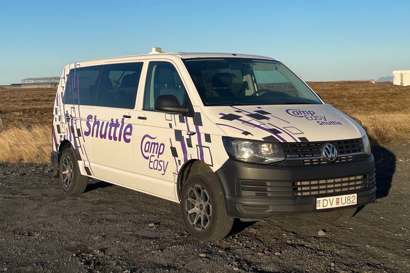 A white Volkswagen van with Camp Easy Shuttle branding, parked on a gravel road in Icelandic terrain.