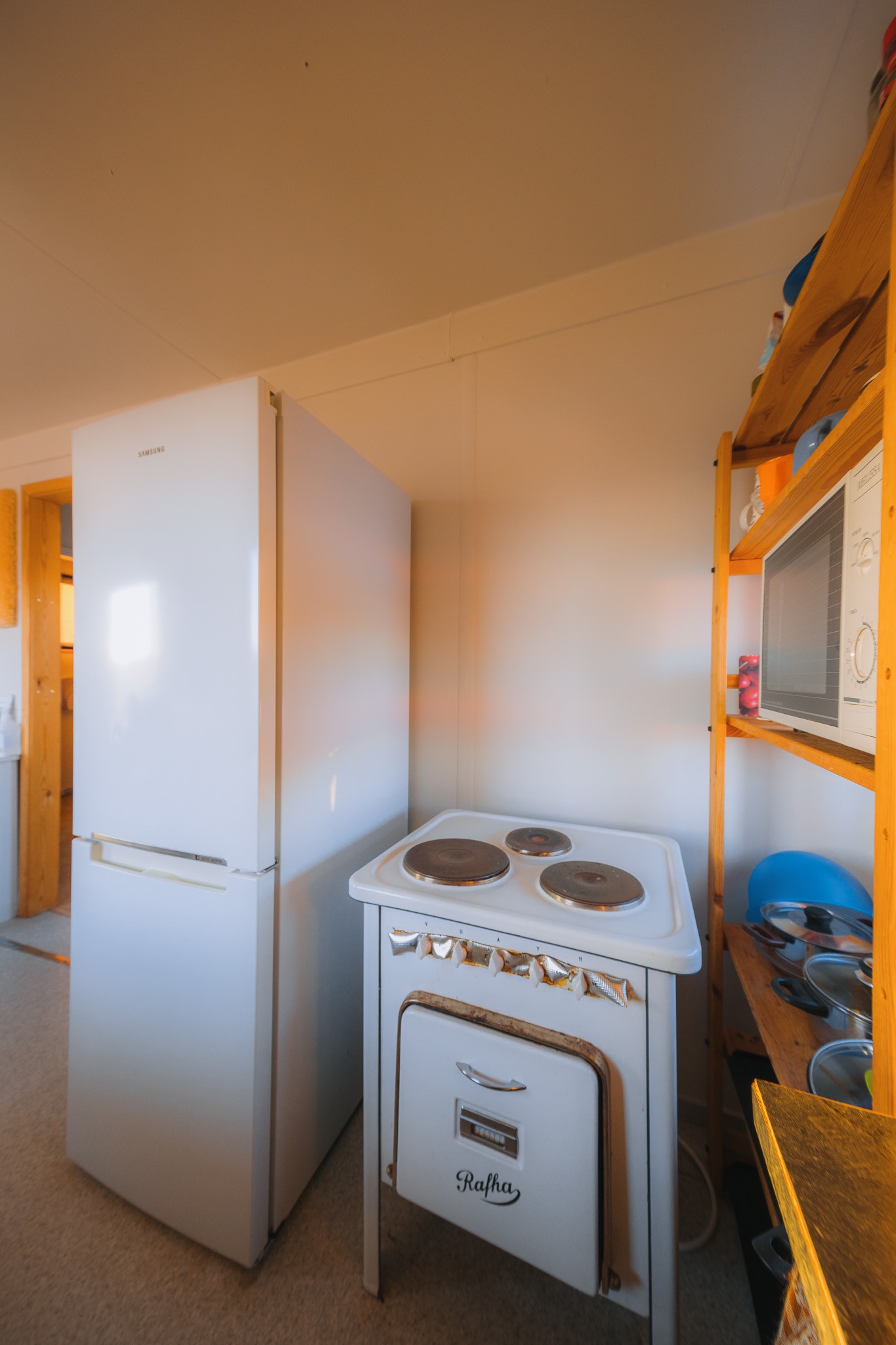 Cozy kitchen corner with a white fridge, vintage stove, wooden shelves, and a microwave.
