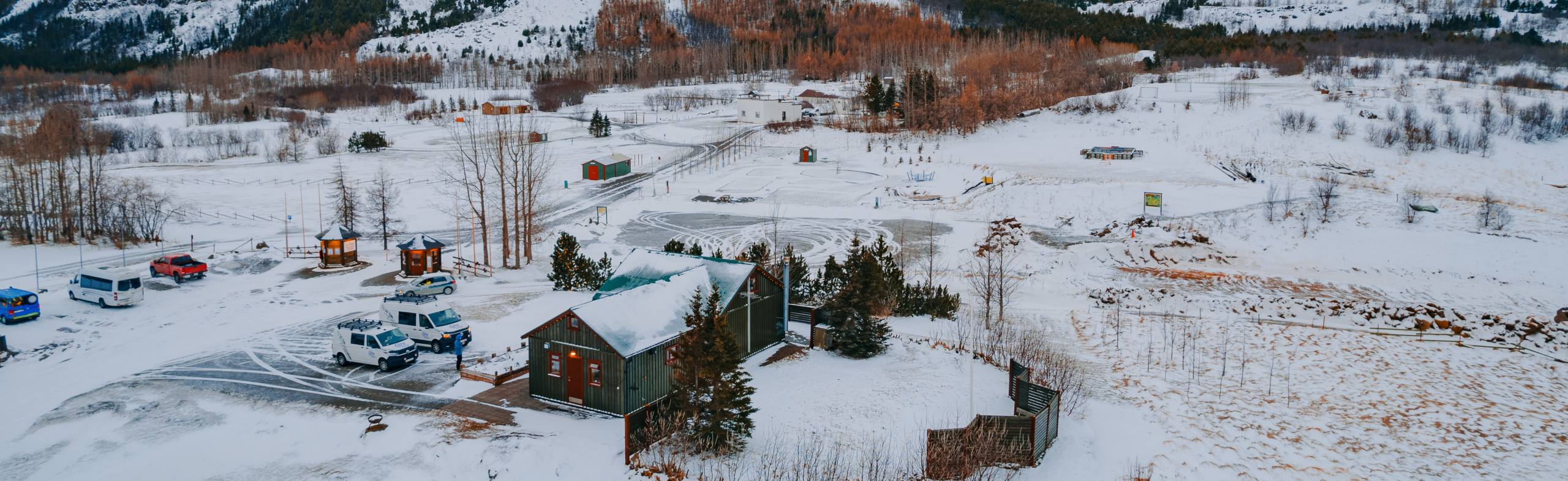 Snow-covered landscape with scattered buildings, vehicles, and evergreen trees.